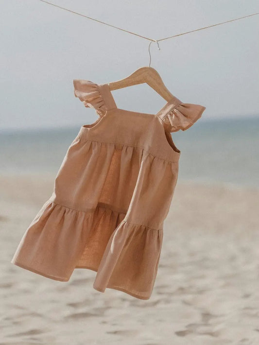 Zachtroze meisjesjurk met ruches hangend aan een hanger op het strand