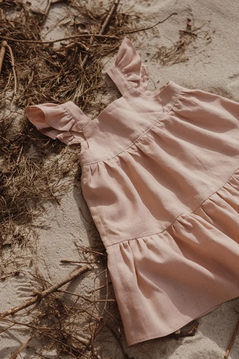 Luchtige zomerjurk voor kinderen liggend op zand met natuurlijke details