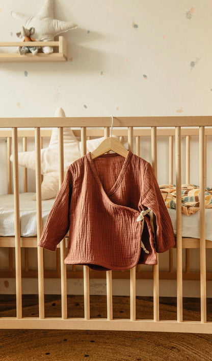 Comfortabele peuter outfit in warme tint bij houten babybed